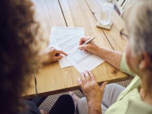 A senior aged woman signing documents with a financial adviser in her home